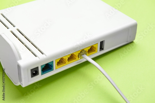Modern wi-fi router and internet cable on green background, closeup