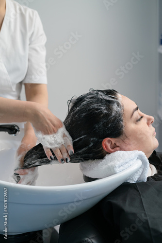 the cosmetologist washes the girl's head with shampoo for further procedures. black hair. plus size.
