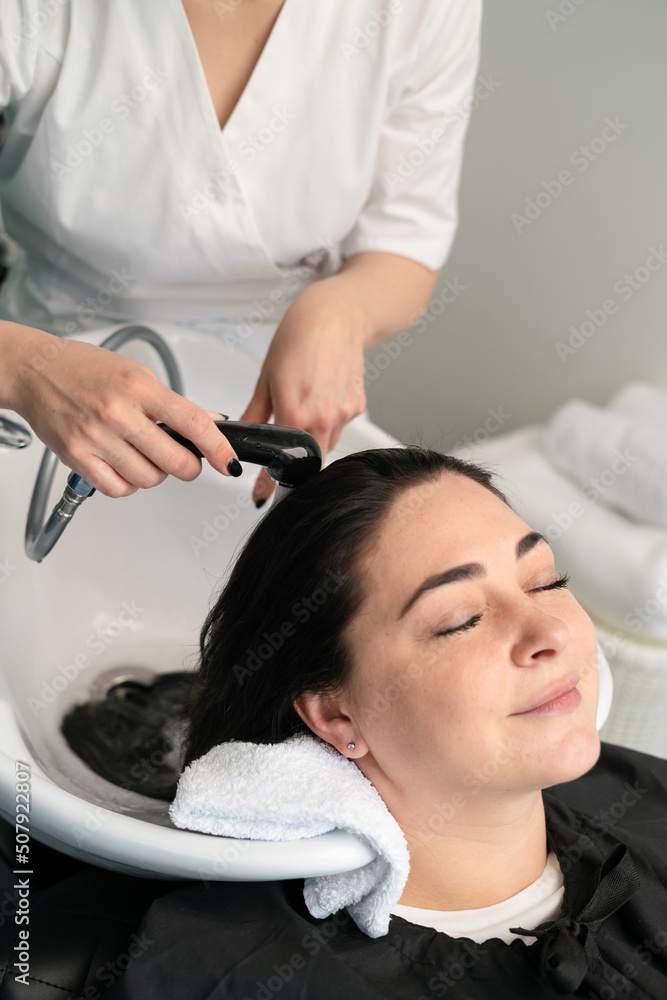 the cosmetologist washes the girl's head with shampoo for further procedures. black hair. plus size. the cosmetologist washes the girl's head with shampoo for further procedures. black hair. plus size.