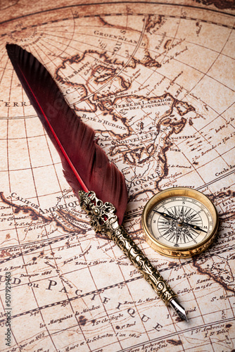 Old feather pen and golden compass on the antique mundi map.