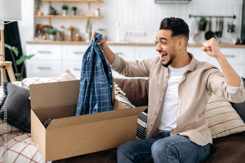 Happy attractive indian or arabian guy opening big carton box, unpacking internet store order at home, contented with fast delivery service and the goods which received, smiling and feel satisfied Happy attractive indian or arabian guy opening big carton box, unpacking internet store order at home, contented with fast delivery service and the goods which received, smiling and feel satisfied