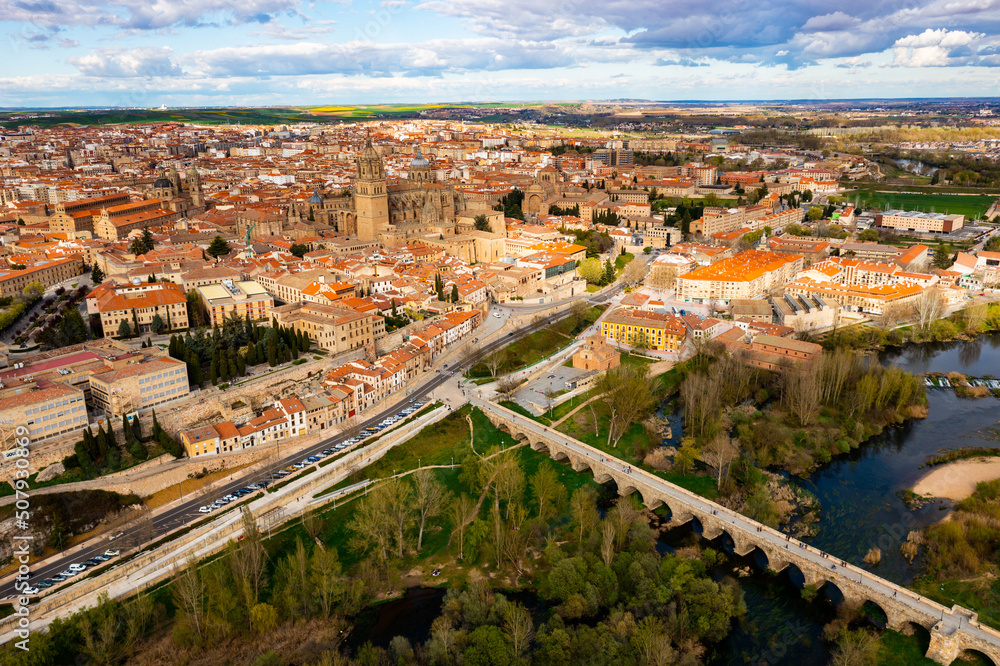 Scenic aerial view of Salamanca historic district overlooking gothic building of cathedral towering over residential buildings and ancient arched roman bridge across Tormes river in spring, Spain