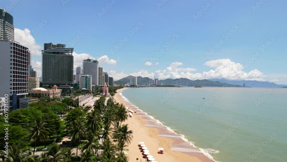 low altitude aerial view of a white sand tropical beach town in asia with white beach umbrellas setup for tourists and tall hotels overlooking the turquoise ocean on a sunny day in Nha Trang Vietnam low altitude aerial view of a white sand tropical beach town in asia with white beach umbrellas setup for tourists and tall hotels overlooking the turquoise ocean on a sunny day in Nha Trang Vietnam