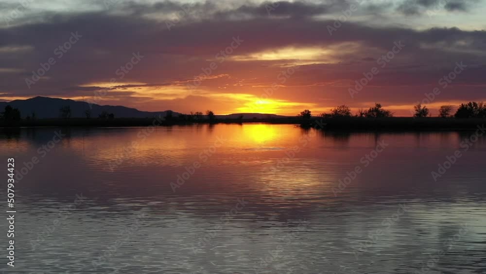 A Lake at Sunset With Cloudy Sunset Reflected in the Water Surface and a Fish Jumping Out of the Water A Lake at Sunset With Cloudy Sunset Reflected in the Water Surface and a Fish Jumping Out of the Water