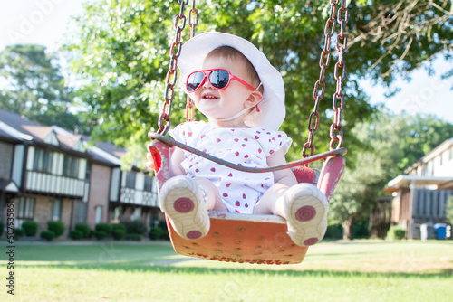 Cute caucasian baby girl toddler on a swing wearing red sunglasses