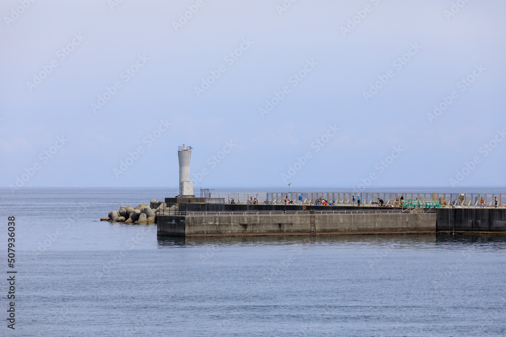 港の灯台と防波堤で釣りを楽しむ人々