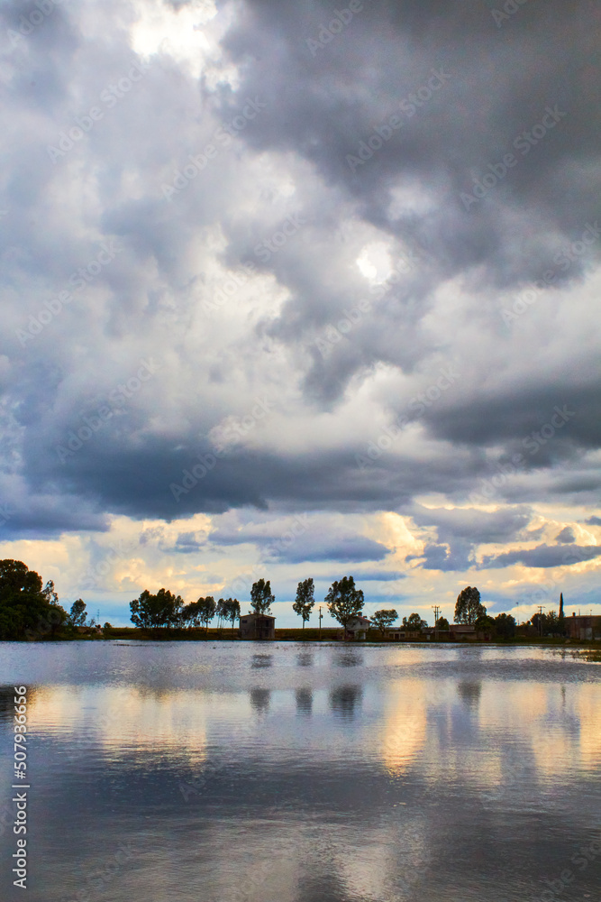 Naklejka premium lake in cloudy day with grey clouds and reflections in the water, rural town in laguna grande zacatecas