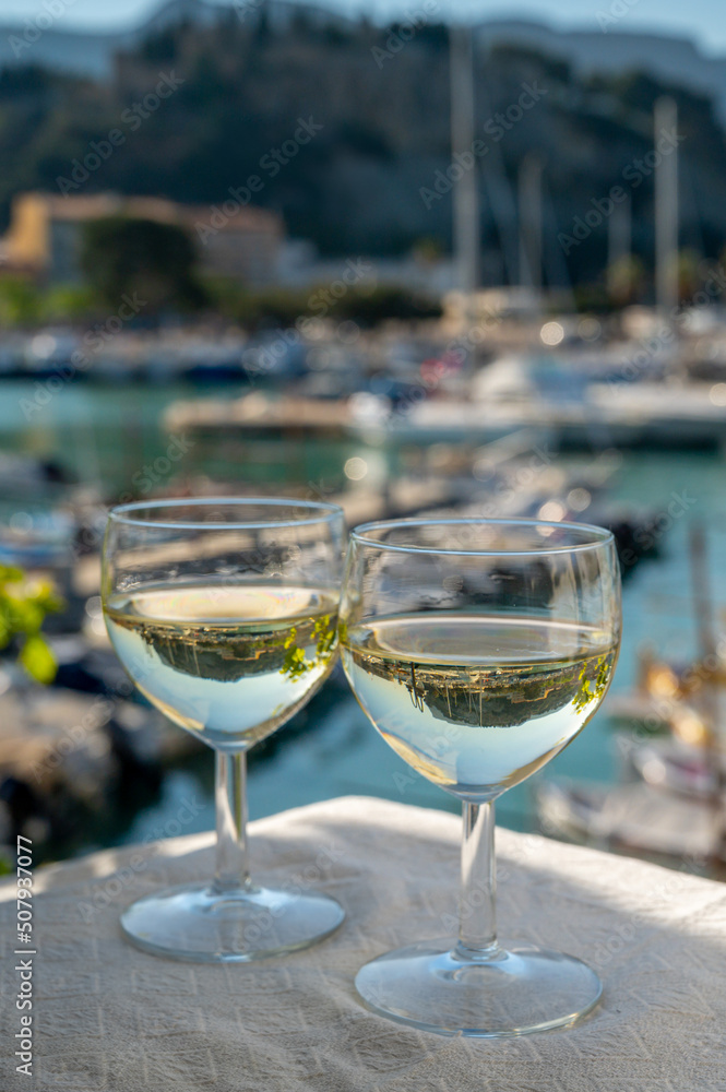 Obraz premium Two glasses of white wine from Cassis region served on outdoor terrace with view on old fisherman's harbour with colourful boats in Cassis, Provence, France