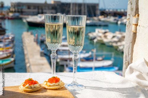 Pairing of blinis with sour cream and salted salmon red caviar and French champagne brut sparkling wine and served with view on colorful boats in harbor of Cassis, Provence, France