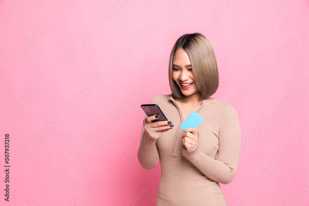 Portrait of a happy young woman showing plastic credit card while using mobile phone shopping online isolated over pink background. Portrait of a happy young woman showing plastic credit card while using mobile phone shopping online isolated over pink background.
