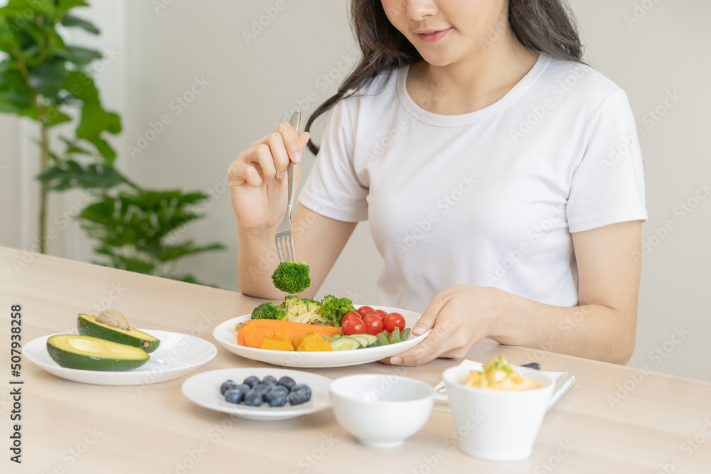 Dieting, diet asian young woman, girl eating, holding fork at broccoli, diet plan nutrition with fresh vegetables salad, enjoy meal on table at home. Nutritionist of healthy, nutrition of weight loss. Dieting, diet asian young woman, girl eating, holding fork at broccoli, diet plan nutrition with fresh vegetables salad, enjoy meal on table at home. Nutritionist of healthy, nutrition of weight loss.