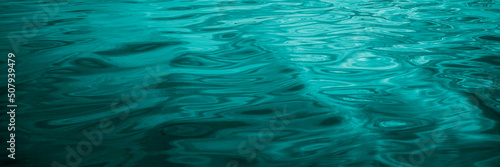 Obraz na płótnie Blue-green water background. Reflection of light on the wavy surface of the water. Ripples. Beautiful teal background with copy space for design. Web banner. Wide. Panoramic. w salonie