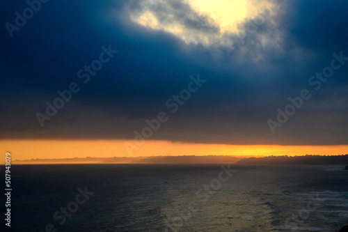 Fototapeta Naklejka Na Ścianę i Meble -  View of the French Basque coast at dawn on a spring day. Below the dark sea on the right side the coast in front a strip of orange color lit like fire that is the coastline, in the sky a large dark gr