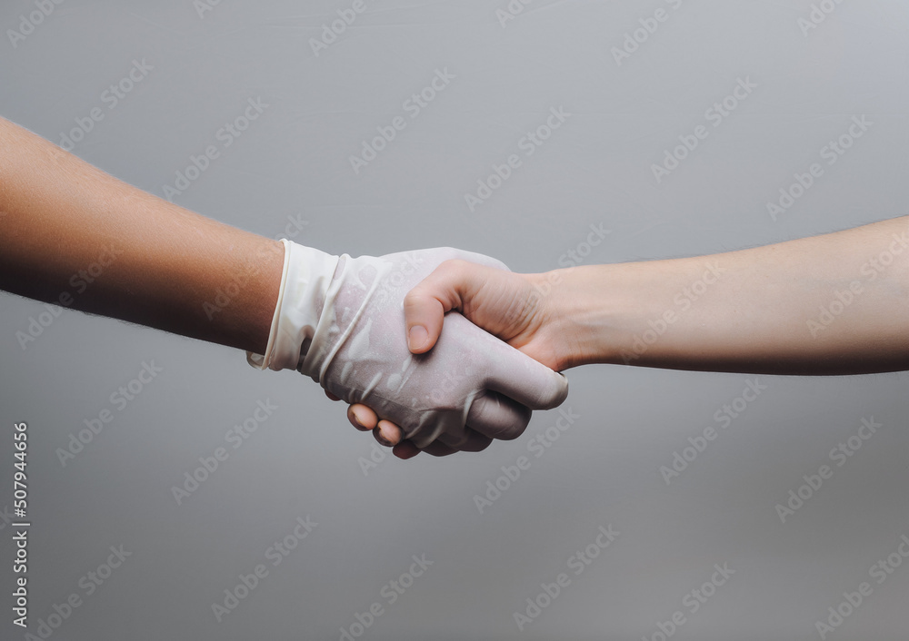 A doctor in a white glove shakes hands with his patient. The concept of interaction and successful treatment. Gray background, copy space. Gynecology. A doctor in a white glove shakes hands with his patient. The concept of interaction and successful treatment. Gray background, copy space. Gynecology.