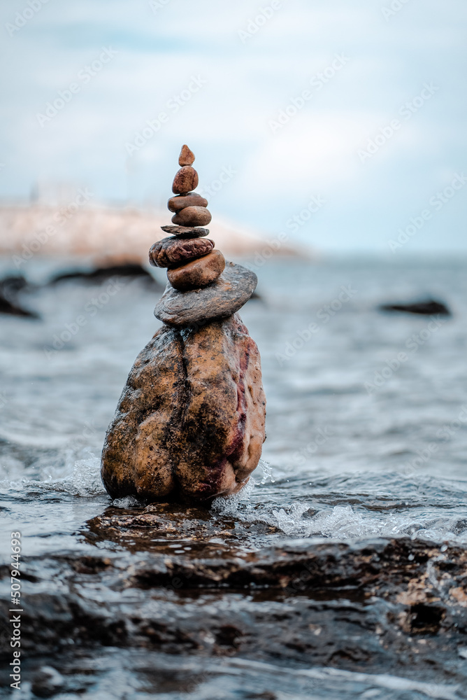 Concept of balance and harmony. Cairn stack of stones pebbles cairn on coast amid the crashing waves. Meditative art of stone stacking