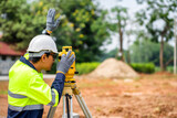 Asian engineers use yellow theodolite to find blueprints at building construction sites.