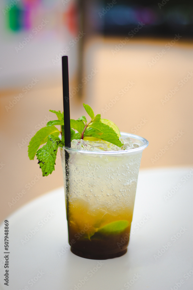 A Plastic glass of Mojito cocktail with lime and mint on white table. A Plastic glass of Mojito cocktail with lime and mint on white table.