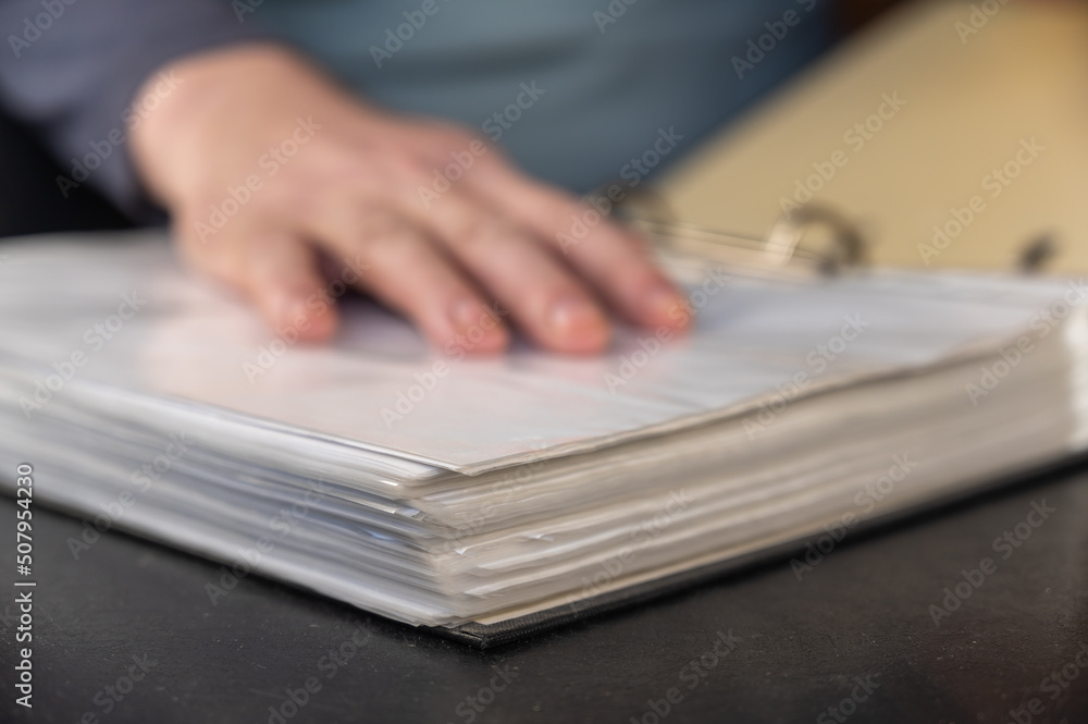 An unfocused shot of a man's hand resting on top of a file folder. Adult Male placed his hand on an open gray folder with a binder. Defocus, noise, grain effect. Selective Focus. An unfocused shot of a man's hand resting on top of a file folder. Adult Male placed his hand on an open gray folder with a binder. Defocus, noise, grain effect. Selective Focus.