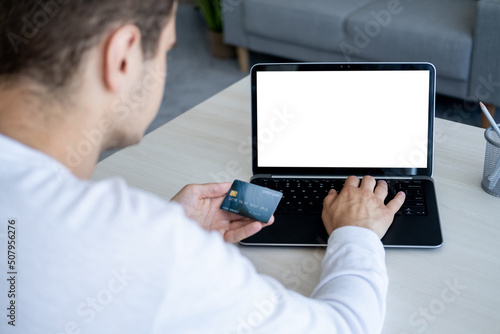 Bank payments. Casual man. Computer mockup. Unrecognizable guy sitting desk with laptop blank screen and plastic credit card in light room interior.