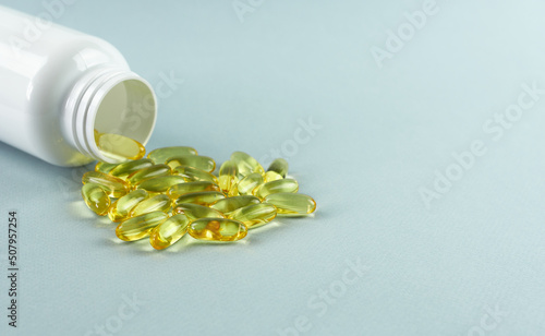 Omega - 3 capsules are scattered on a blue background next to a white bottle. 