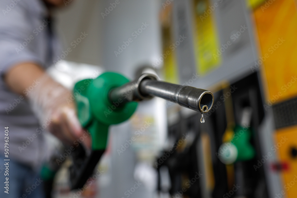 Fototapeta premium Shallow depth of field (selective focus) details with a man holding a fuel pump dripping with gasoline in a gas station.