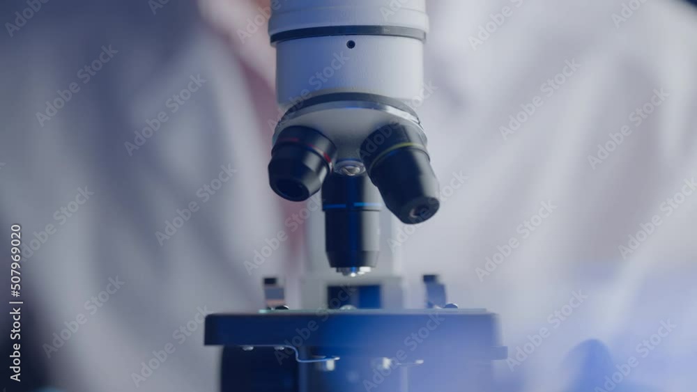 Virologist or scientist is looking into microscope. Biochemical research. Scientific and medical lab instrument. A doctor is search for vaccine to treat diseases in biohazard laboratory Virologist or scientist is looking into microscope. Biochemical research. Scientific and medical lab instrument. A doctor is search for vaccine to treat diseases in biohazard laboratory