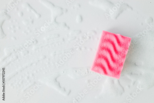 Pink sponge with detergent foam on white background, close up. Cleaning concept