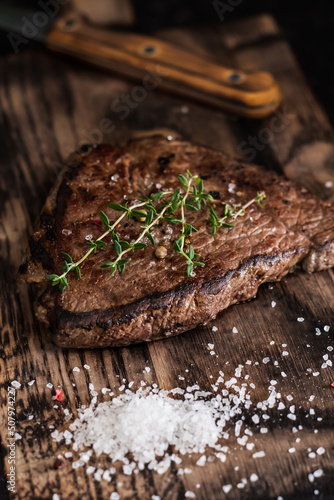 Beef tenderloin steak with salt and herbs on a wooden board on a dark background