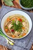 Chicken soup with noodles and vegetables in a white bowl on a rustic wooden background