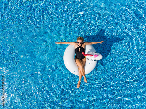 Aerial top view from above of woman on unicorn pool float in pool. Enjoying summer vacations during quarantine.