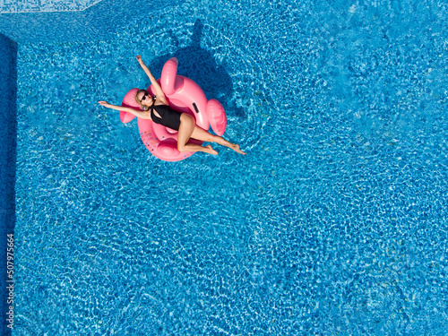 woman on flamingo pool float in pool in the sea, drone aerial view. Summer holidays