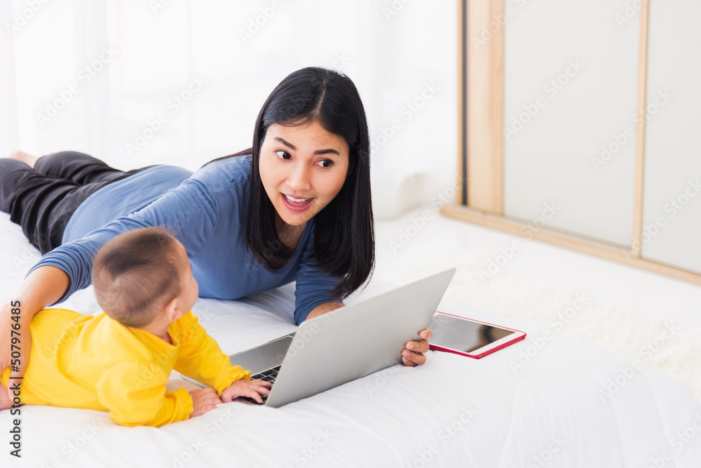 Fototapeta premium Asian new young beautiful mother finding and reads information on a laptop for milk mixing on a bottle in the bedroom at home