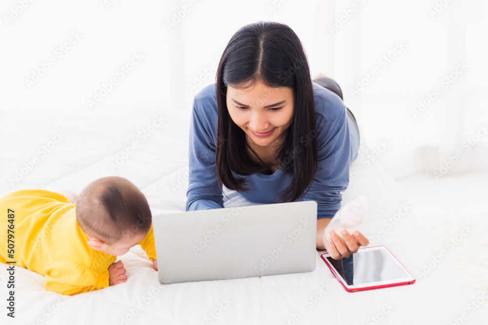 Asian new young beautiful mother finding and reads information on a laptop for milk mixing on a bottle in the bedroom at home Asian new young beautiful mother finding and reads information on a laptop for milk mixing on a bottle in the bedroom at home
