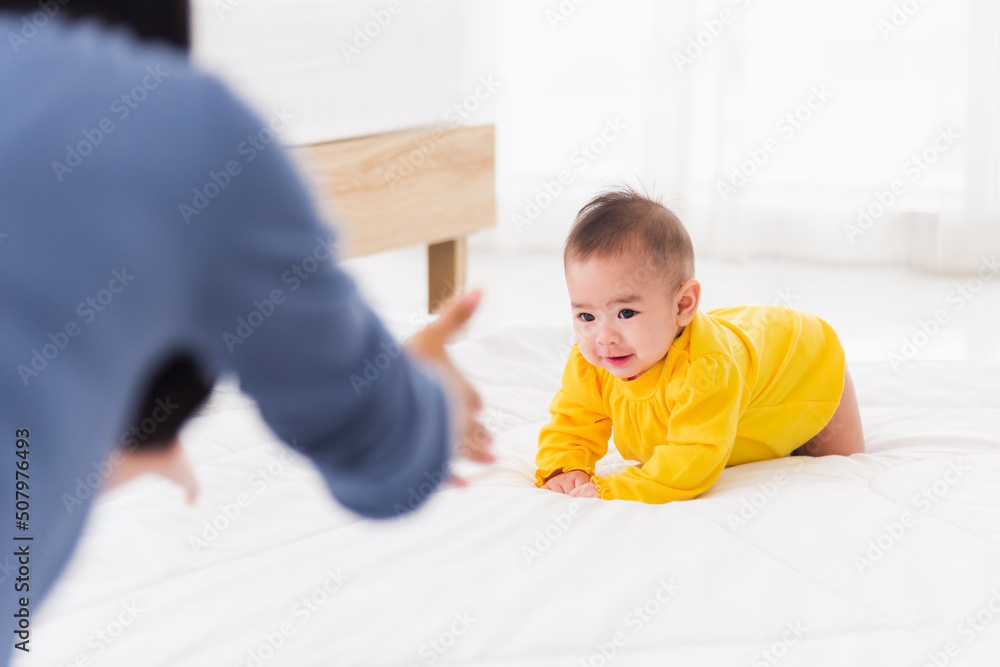 Asian happy young mother have fun learn walking crawling his daughter baby indoors bedroom at home. The mom playing with her little baby to crawl, two family Asian happy young mother have fun learn walking crawling his daughter baby indoors bedroom at home. The mom playing with her little baby to crawl, two family
