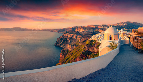 Fototapeta Naklejka Na Ścianę i Meble -  Small chapel on Santorini island. First sunlight glowing empty street of Thira resort, Greece, Europe. Traveling concept background.