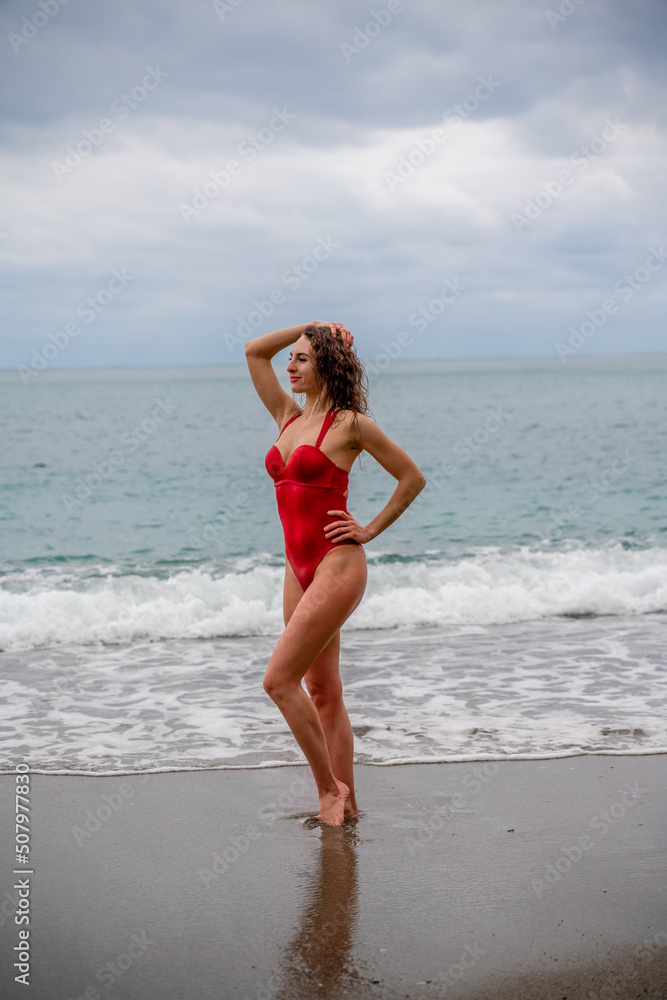 A beautiful and sexy brunette in a red swimsuit on a pebble beach, Running along the shore in the foam of the waves A beautiful and sexy brunette in a red swimsuit on a pebble beach, Running along the shore in the foam of the waves