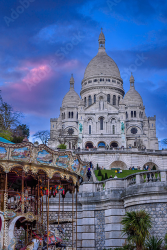 Purple twilight above the Sacré-Coeur Basilica on the top of the Montmartre hill in Paris, France with a carousel in the foreground.