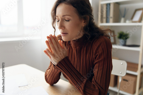 Suffering after shocked news about family crying upset sad curly beautiful woman folds hands in pray asks God's help have depressive mood or problems in relations at home office. Copy space