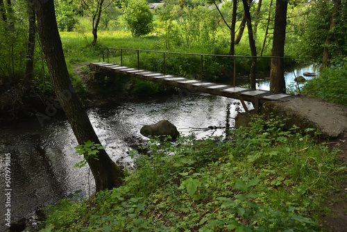 Bridge over a small forest river with green, beautiful banks, in spring