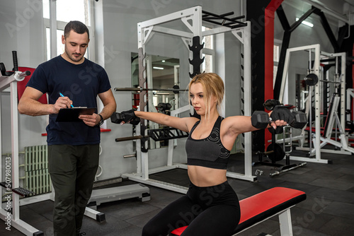 male trainer help her woman client working with dumbbell weights at gym