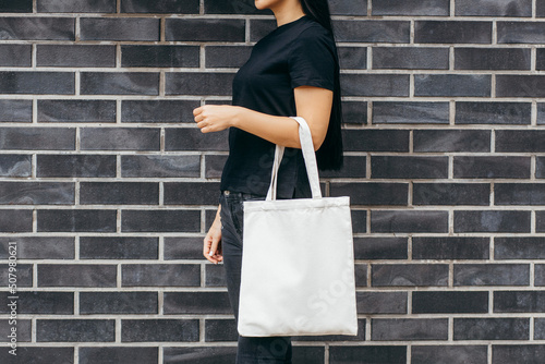 Young asian model girl dressed in a black t-shirt on the street holding white eco bag, mock up