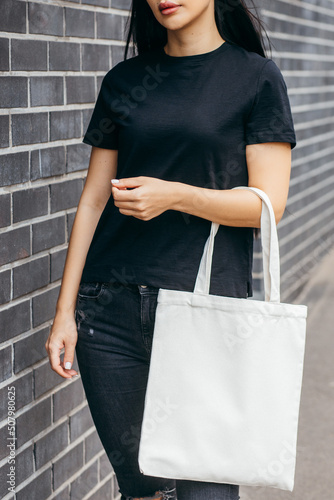 Young asian model girl dressed in a black t-shirt on the street holding white eco bag, mock up