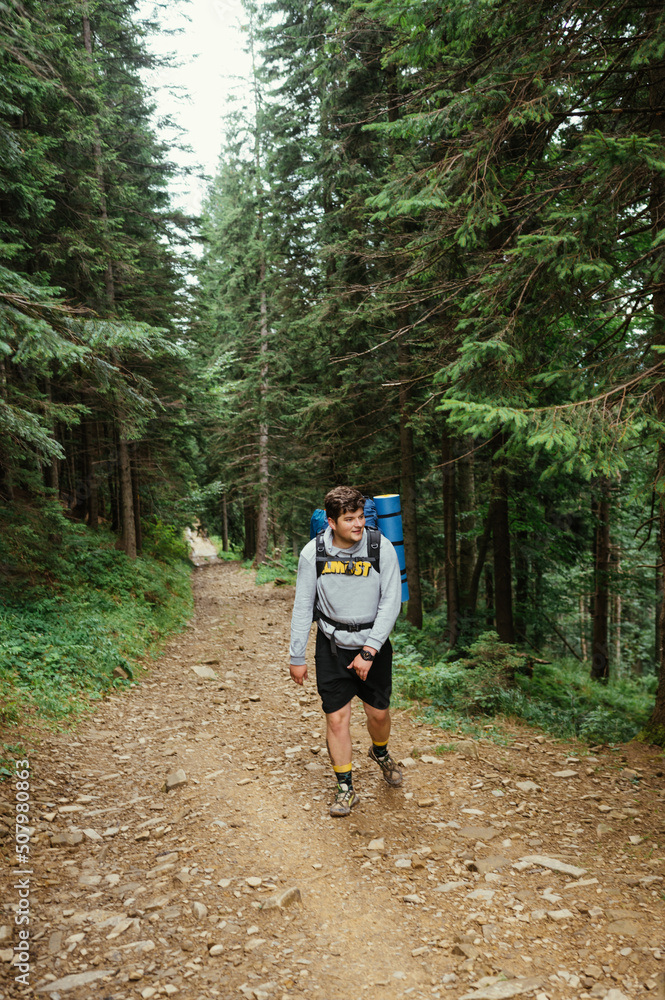 Male hiker in casual clothes with a backpack on his back goes to the mountains on a trail through the woods. Vertical Male hiker in casual clothes with a backpack on his back goes to the mountains on a trail through the woods. Vertical