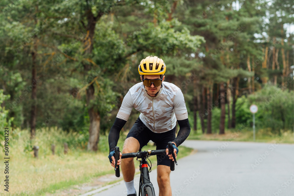 Obraz premium Male professional cyclist in sportswear rides out of town on an asphalt road with a serious face.