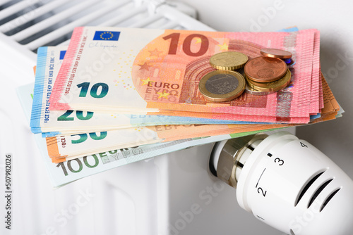 Euro money banknotes on heating radiator battery with thermostat temperature regulator. Concept of expensive heating costs and rising gas energy bill prices for winter cold season.