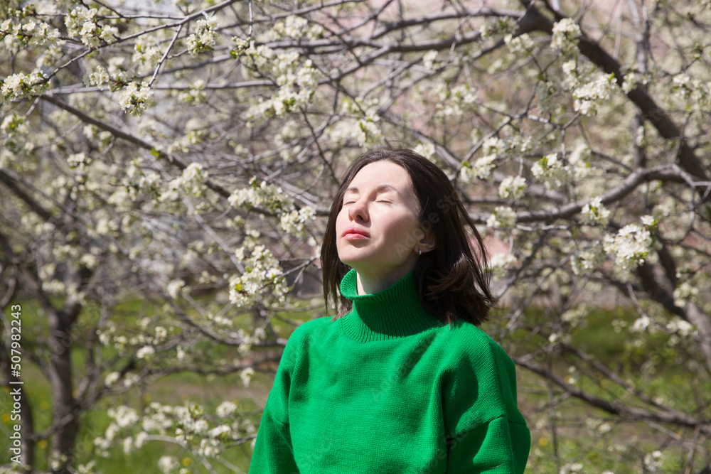 woman in green sweater with short hair blowing in the wind in flowering spring garden. Spring awakening. Slow life. Enjoying the little things. Dreaming of spring. woman in green sweater with short hair blowing in the wind in flowering spring garden. Spring awakening. Slow life. Enjoying the little things. Dreaming of spring.