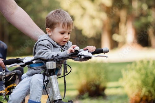 Cute little caucasian boy sitting on beach by father bicycle. Family weekend in countryside