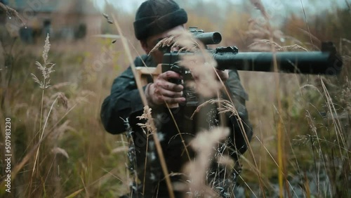 Army sniper sitting and aiming in grass carrying his rifle. photo