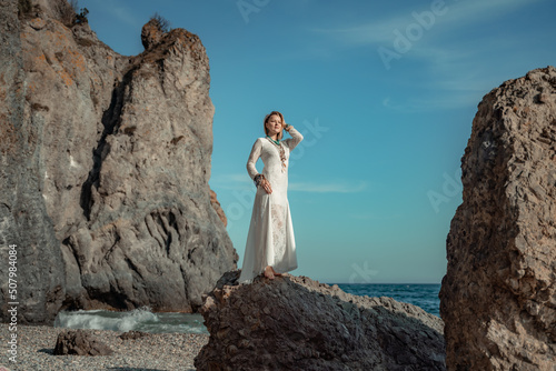 Middle aged woman looks good with blond hair, boho style in white long dress on the beach decorations on her neck and arms.