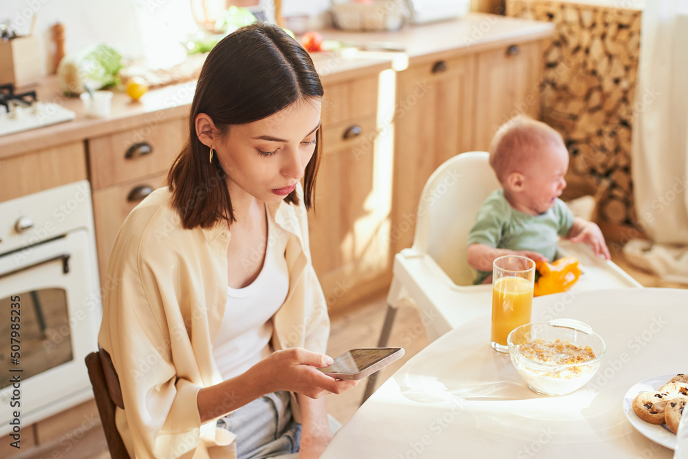 A young mother uses a smartphone while her young son cries.